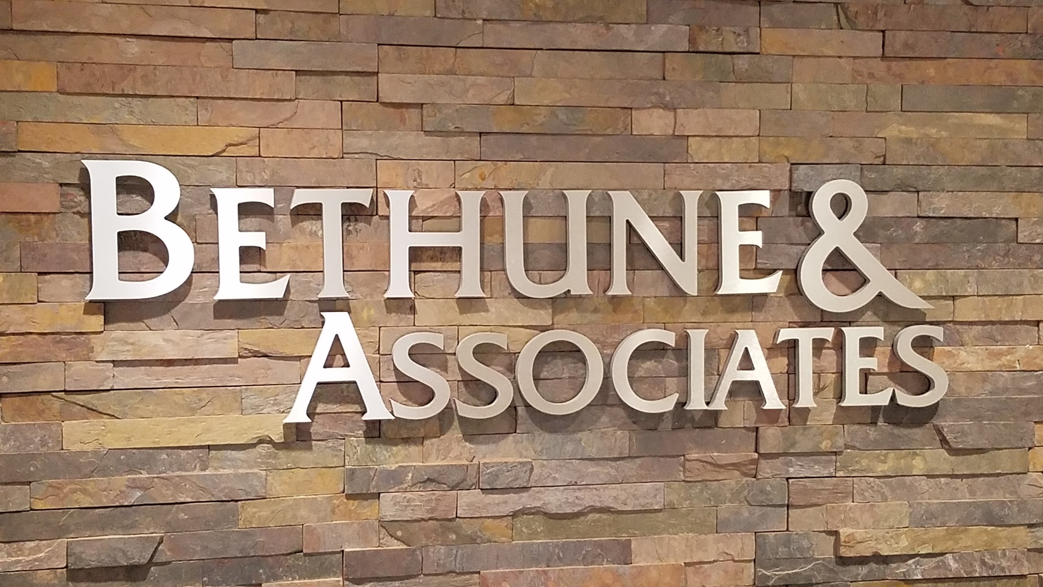 The Bethune & Associates office sign: polished metal serif lettering mounted on a warm stacked-stone wall